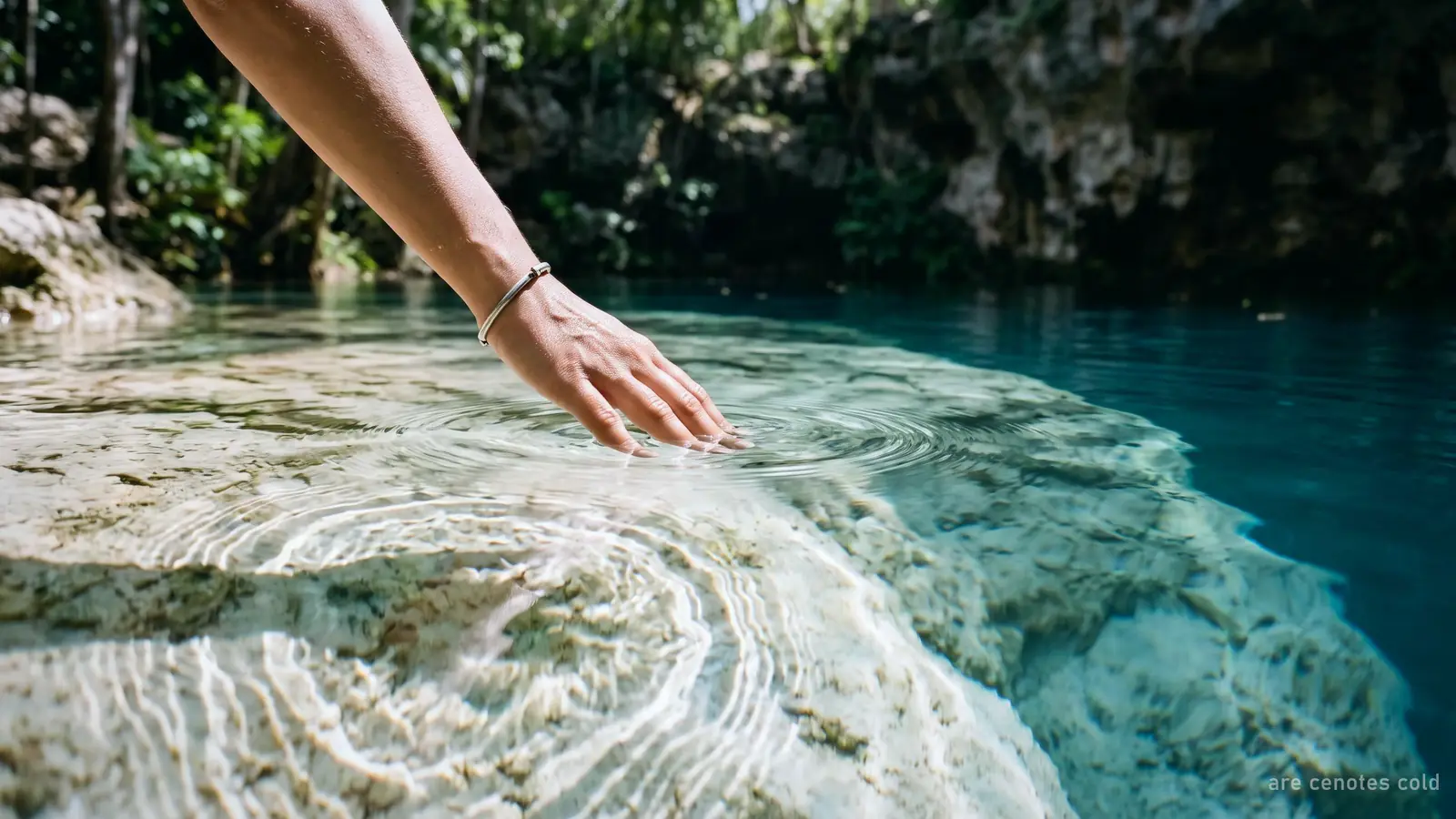 A hand touching the clear water of a cenote over white limestone